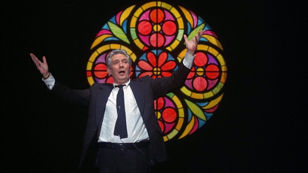 Peter Finch standing in front of a stained glass window in Network.